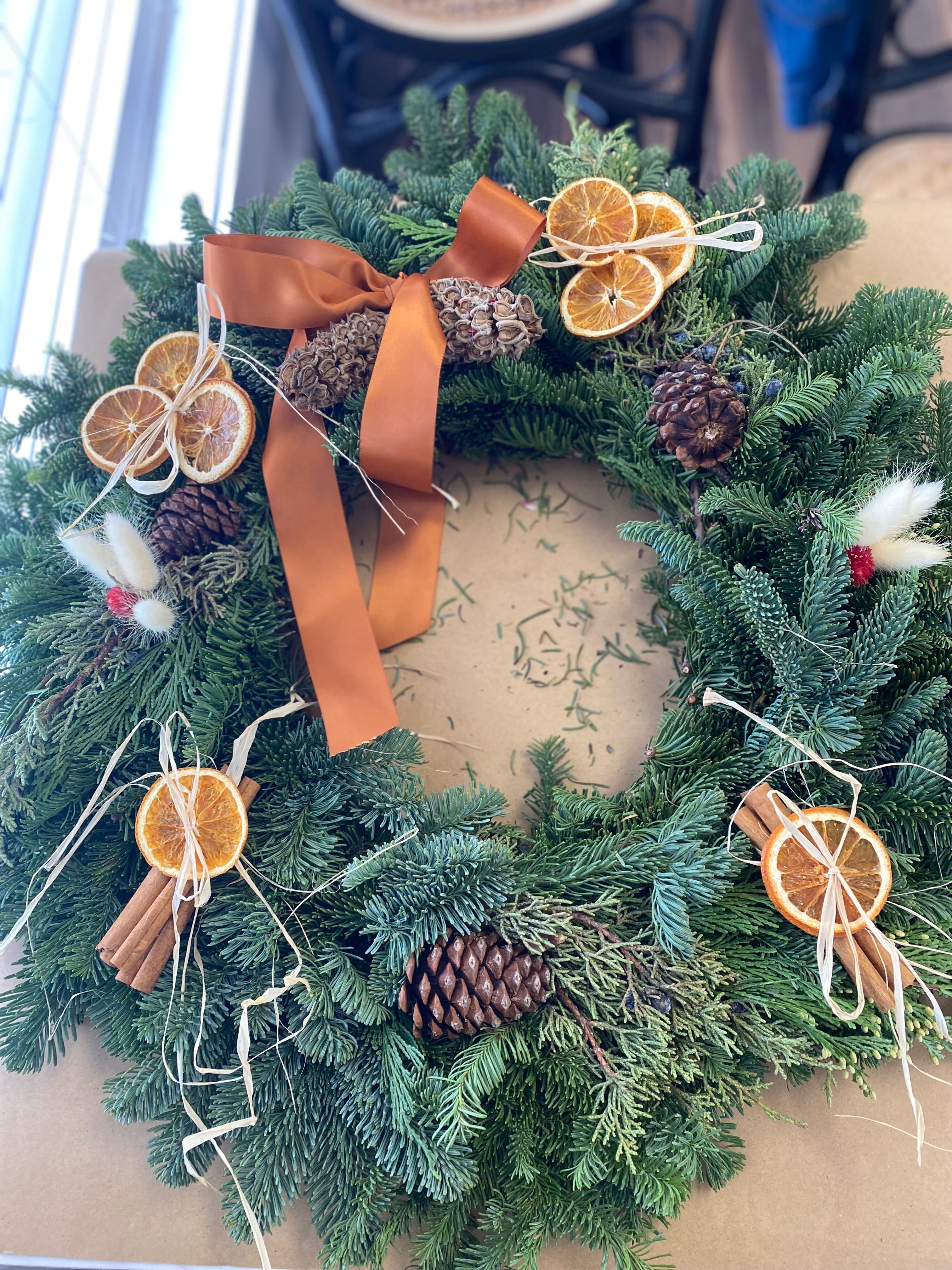 Christmas wreath with pine cones, dried oranges, and ribbons on a neutral background