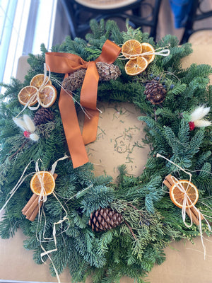 Christmas wreath with pine cones, dried oranges, and ribbons on a neutral background